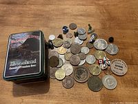 Overview of coins, pins, and tin box on wooden surface showing variety of items and Moosehead Beer tin.