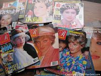 Photo displaying multiple Royalty magazines featuring Princess Diana on the covers arranged fanned out on a wooden surface.