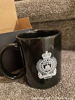 Black ceramic coffee mug with white Kingston Police logo and text.
