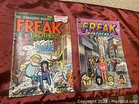 Photo of two comic books The Fabulous Freak Brothers Issues #1 and #4 showing front covers laid flat on a red fabric.