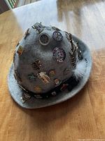 Gray vintage Capo Austria waterproof hat with white feather and various pins including Oktoberfest, ski, shields, and other assorted designs.