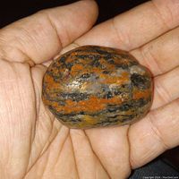 Polished Canadian banded jasper stone held in hand, showing the textured orange, black, and white banding on one side.
