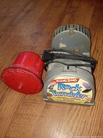 Photo showing the Rolling Stones rock tumbler machinery with the red barrel attached and power cord wrapped on the motor base.