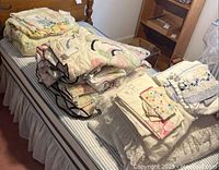 Photo showing twin bed with assorted folded bed linens, blankets, and pillow covers stacked on top.