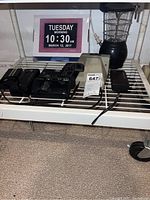 Full view showing digital clock with time and date display, two film cameras, and a vintage lantern on a white metal rack.