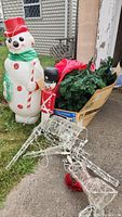 Photo of Christmas tree box with dismantled branches, blow-mold snowman, blow-mold soldier, and lighted wireframe reindeer outside.