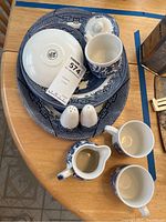 Full view of set on wooden table including plates, platter, mugs, creamer, and salt and pepper shakers.