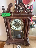 Full front view of the wooden clock showing its decorative carved frame with finials and scrollwork on top.