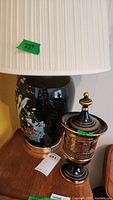 Full view of the Asian influence jar-shaped lamp with bird and floral design along with covered urn vase with gold trim on a wooden surface.