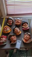 Overview of all nine character head wall decor pieces laid out on table with window light.