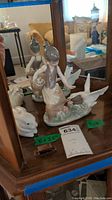 Lladro girl with swan figurine and one white rabbit figurine in the background, shown on wooden surface with mirror reflection