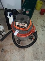 Front angle view of Ridgid wet dry vacuum showing motor housing, power cord, hose, and caster wheels.