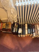 Wide shot showing the books lined up on the floor next to a radiator and curtain, showing thickness and dust jackets