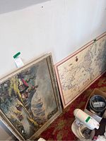 View of landscape painting and large map leaning against wall on carpeted floor.