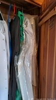 Dresses and gowns hanging closely together including a white gown in plastic, a green dress, and a black dress.