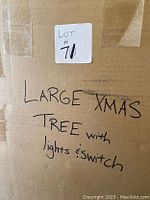 Cardboard box side with handwritten label stating: 'LARGE XMAS TREE with lights & switch' and lot number 70 tag visible.