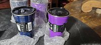 Close-up photo of four reusable plastic cups in blue and purple colors with black lids.