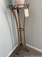 Tall brass plant stand with glass top and vase on top corner view