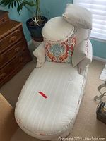 Chaise lounge with light beige upholstery and one multicolor ornamental pillow