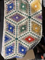 Quilt spread out showing colorful hexagonal floral patchwork designs in blue, green, yellow, purple and red with a white background and green chain border detail.