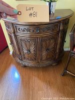 Front view of ornate wooden entryway chest showing flower-like carved designs and curved shape.