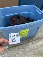Blue storage bin with three round wicker flower pot rollers inside. Each roller has four caster wheels attached to the bottom.