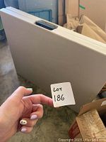Photo showing the folded rectangular table held upright revealing the white surface and thickness.