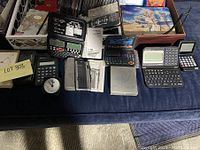 Multiple electronic calculators, including a flip calculator, shown with instruction manuals and user guides on a blue cloth surface.