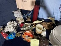 Overview of various nautical decor items on dark blue fabric background including coral, glass fish, ceramic animals, candles, and tureen.