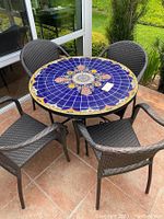 Full view of round tile mosaic patio table surrounded by four resin wicker chairs.