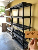 Photo of a black plastic storage shelving unit with five shelves placed inside a garage.