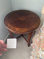 Front angled view of the round wooden side table showing the wood grain and sunburst inlay on the top.