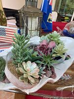 Top-side view of the artificial succulent arrangement inside a clam shell container with surrounding background items.