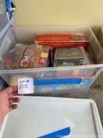 Plastic bin with various vintage toys inside including wooden blocks and boxed toy sets.