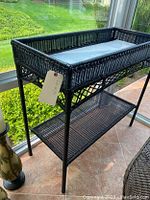 Full view of black wicker console table showing rectangular shape with raised edge top shelf and lower open shelf, set near window.