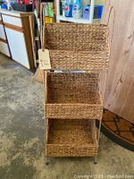 Front angle view of the three-tier wicker shelving unit on metal stand with tags attached