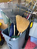 Various views of used yard tools including rakes, broom, shovels in gray plastic trash can. Items arranged with handles protruding.