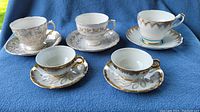 Front view of 5 teacups with matching saucers showing gold floral and turquoise trim decorations.