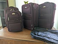 Four pieces of Air Canada branded luggage in dark burgundy/maroon, with one black hanging suit bag laid out on a surface.