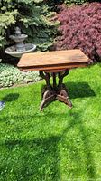 Full view of the antique wooden accent table on grass outdoors, showing rectangular top and ornate carved base.