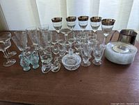 Full assortment of the lot including stacked small plates, crystal glasses with etched designs and silver rims, covered candy dish, and stainless steel pitcher.