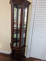 Front and side view of a tall, dark solid wood display cabinet with glass panels and shelves.