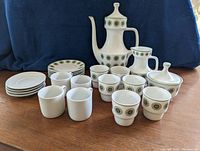 Full set of white porcelain espresso pieces with green circular pattern and gold trim: coffee pot, creamer, sugar bowl, ten cups and ten saucers on display.