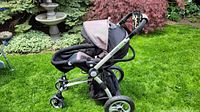 Side view of Gugu black stroller on grass showing canopy, cushioned seat, storage basket, and four wheels.