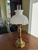Full view of the brass lamp showing the octagonal base, polished column, and white glass shade with ruffled chimney top.