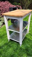 Full view of kitchen island cart showing butcher block top, white frame, and lower stainless steel shelves
