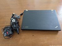 Closed Lenovo ThinkPad T420 laptop with charger and wired pointing device coiled beside it on a wooden surface.