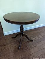 Round solid wood side table showing the full tabletop and pedestal base from a side angle on hardwood floor.