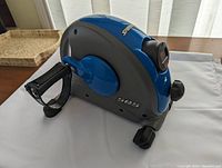 Blue and gray compact stepper with digital monitor and adjustable resistance knob, side view showing one pedal with strap.