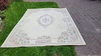 Top view of the whole cream wool rug laid on grass showing central floral medallion and border floral design.